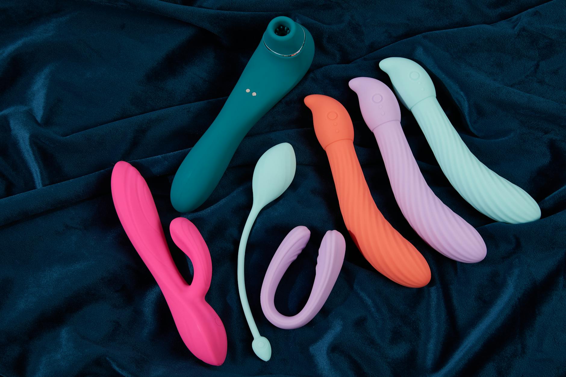 Vibrant collection of silicone sex toys in various colors displayed on dark fabric