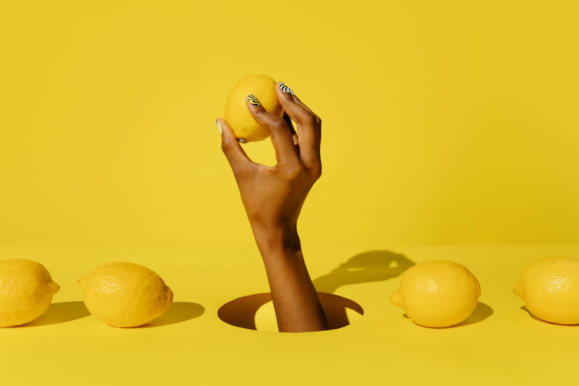 A hand holding a fresh lemon against a bright yellow background, symbolizing renewal and the return to pleasure