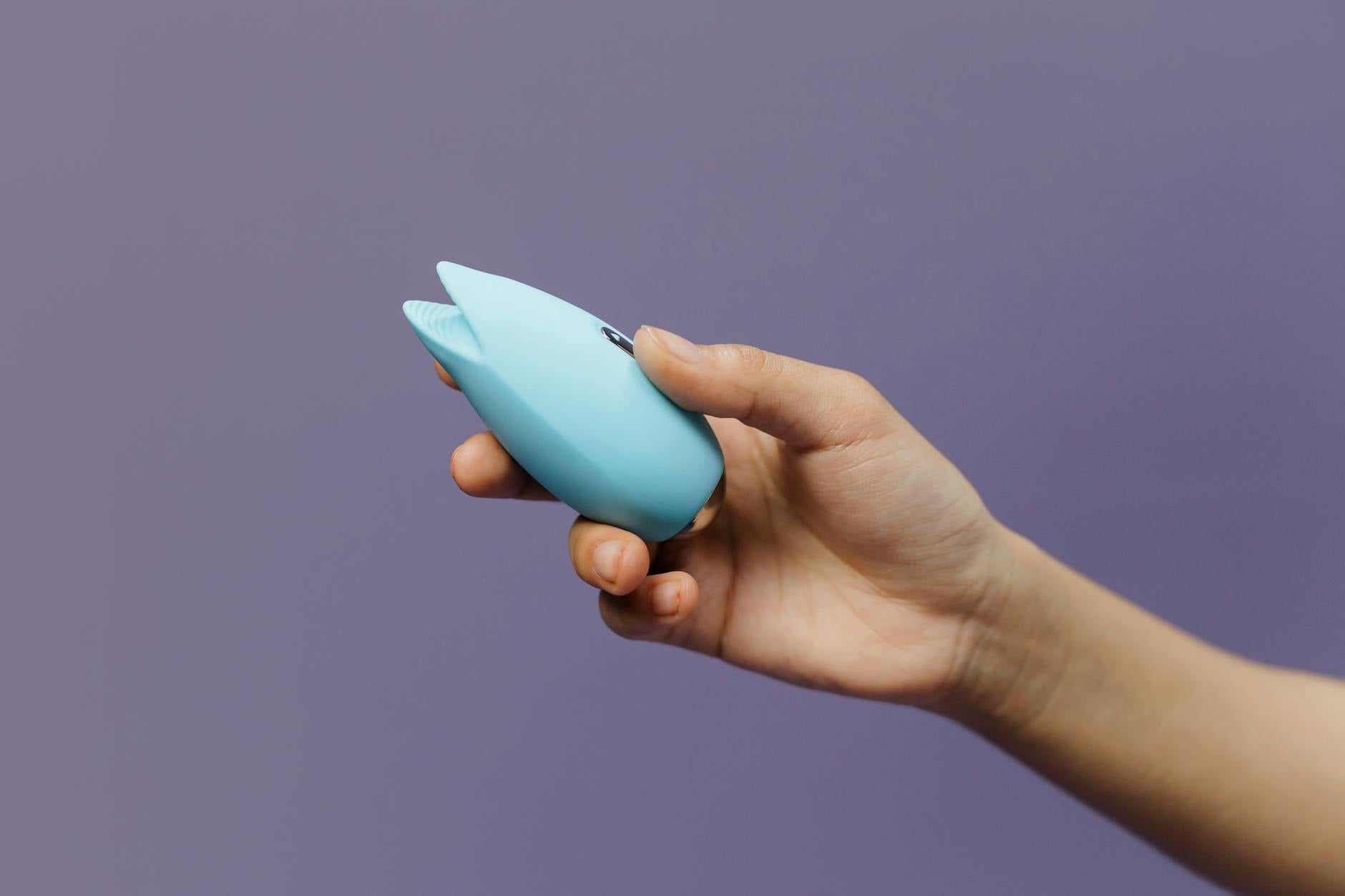 A lemon clitoral vibrator held in hand against a purple background