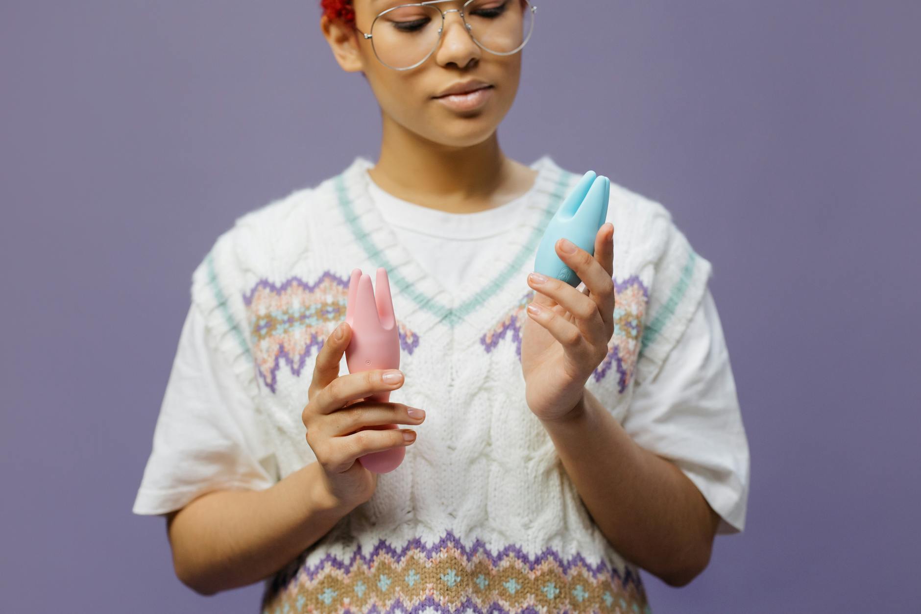 Woman holding blue and pink silicone vibrators thoughtfully, representing gentle pleasure options for sensitive bodies