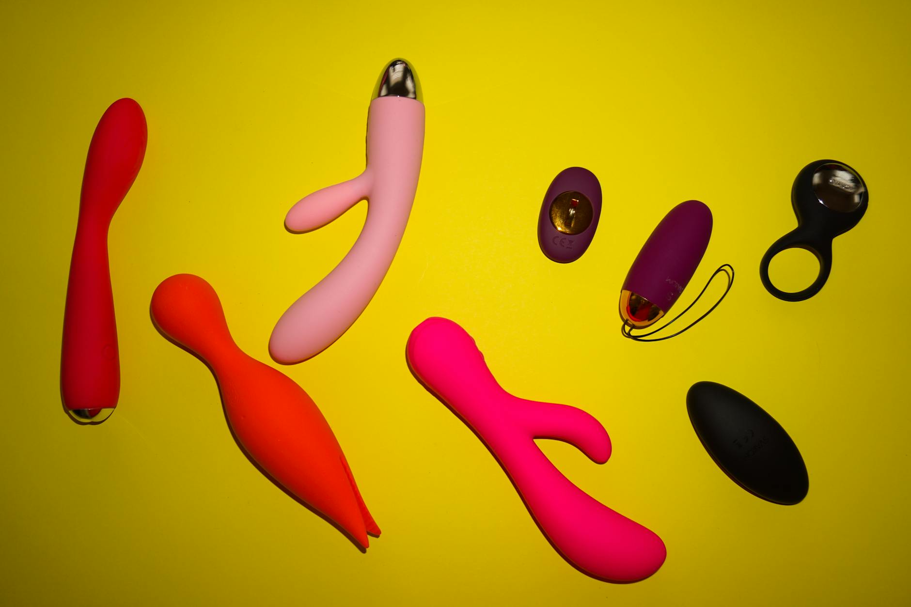 Two hands reaching over a variety of colorful sex toys arranged on a table, representing partnership and exploration.