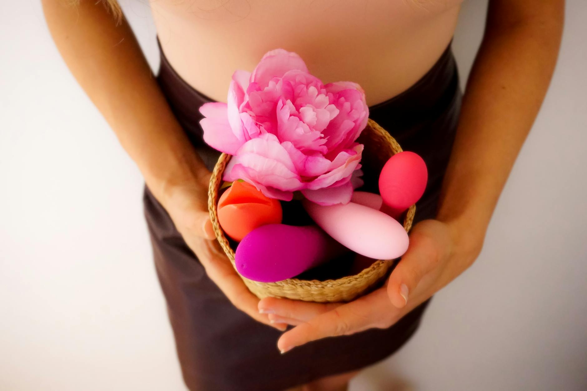 Basket of colorful vibrators and wellness products on a neutral surface